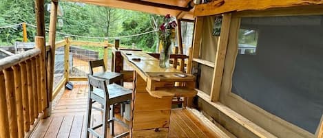 A wooden deck with a table and chairs, a small bar area, and a large window.