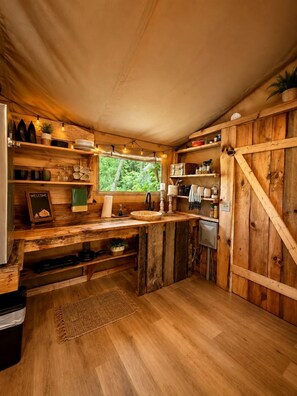 A rustic kitchen with wooden shelves, a sink, and a window overlooking greenery.