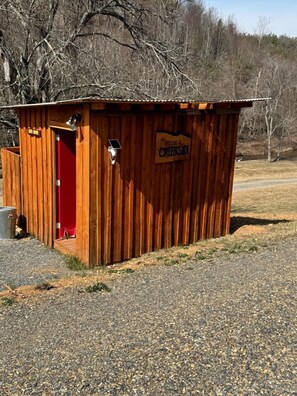 A wooden structure with a red door, a sign reading 'Welcome to Creekside,' and a solar-powered light fixture. - Creekfront Safari Tent with Outdoor Bath and Deck in Virginia (Hillsville)