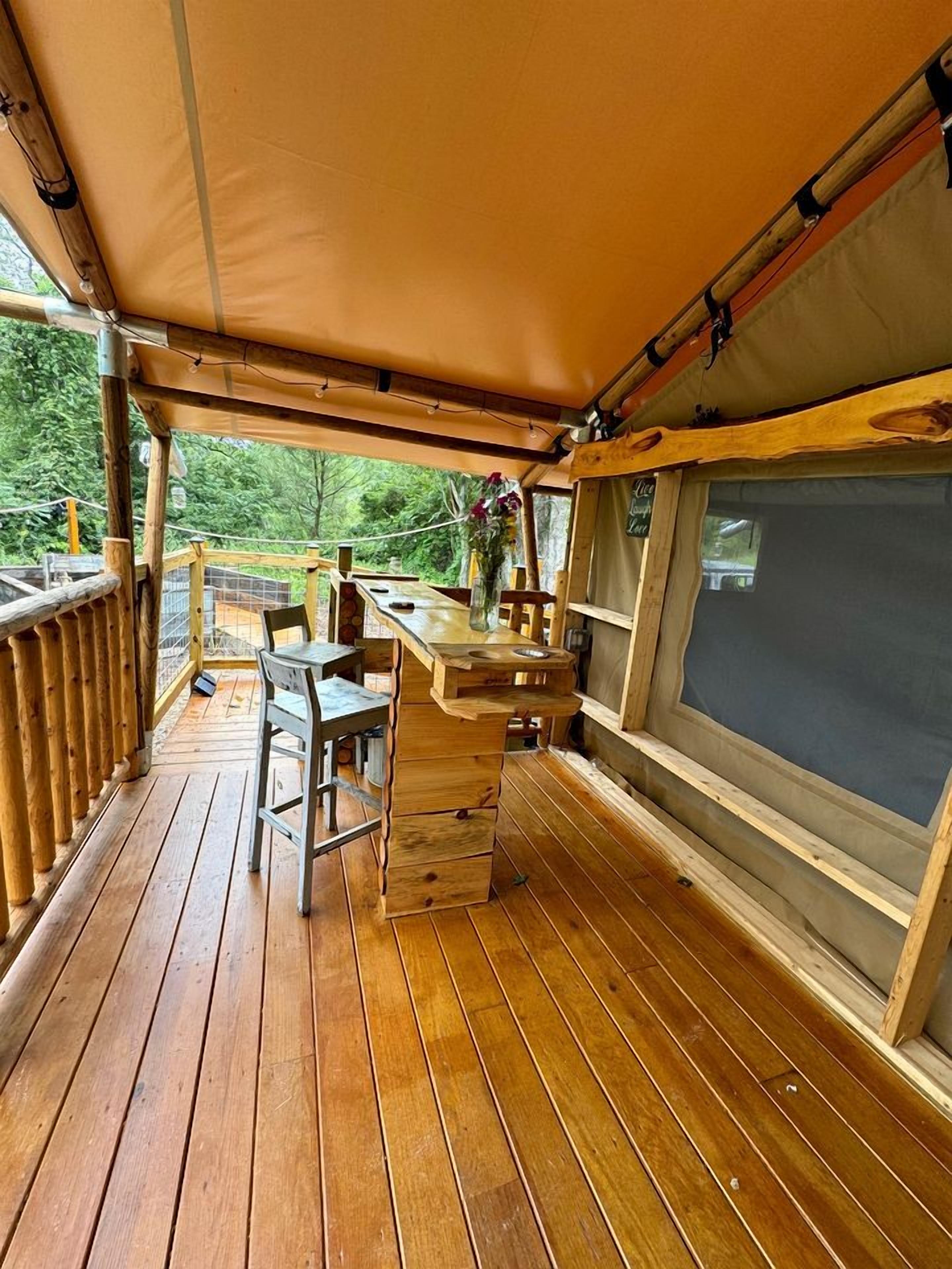 Une terrasse en bois avec une table et des chaises, un petit coin bar et une grande fenêtre.