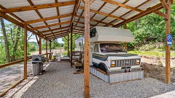 A covered RV parking area with a gravel floor, wooden benches, and a trash can.