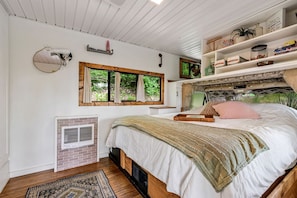 Une chambre à coucher avec un lit, une fenêtre, une étagère remplie de livres et un petit radiateur.