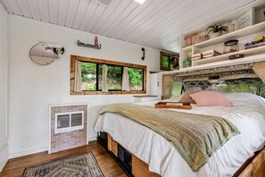 A bedroom with a bed, a window, a shelf with books, and a small heater. - Gorgeous Caravan Glamping Escape for Four in Dover, Ohio (Dover)
