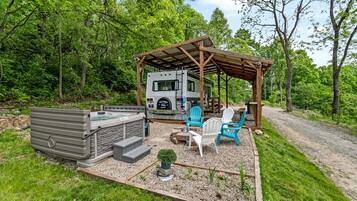 A recreational vehicle with a covered patio area, outdoor seating, and a hot tub.