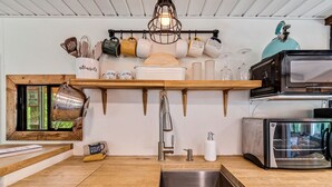 Ett kök med en diskho i rostfritt stål, en brödrost från Proctor Sloane och ett hängande hyllsystem för köksredskap och olika typer av muggar.