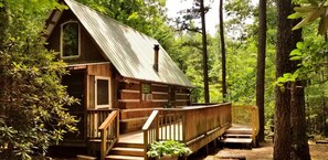 A rustic cabin with a wooden exterior, a metal roof, and a wooden deck. - Romantic Log Cabin with Hot Tub near Cherokee National Forest, Tennessee (Coker Creek)