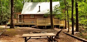 A cabin with a deck, surrounded by trees. - Romantic Log Cabin with Hot Tub near Cherokee National Forest, Tennessee (Coker Creek)