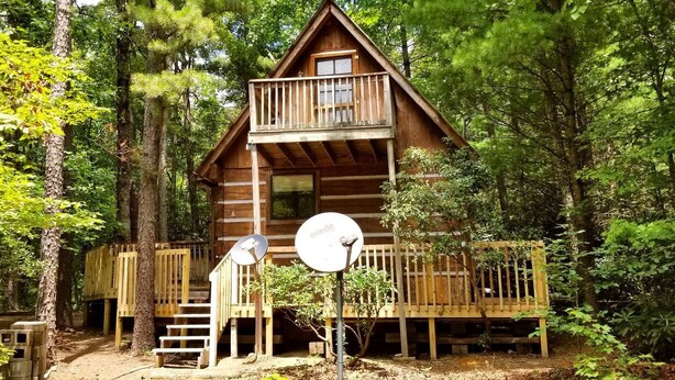 A cabin with a balcony, surrounded by trees. - Romantic Log Cabin with Hot Tub near Cherokee National Forest, Tennessee (Coker Creek)