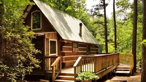 A rustic cabin with a wooden exterior, a metal roof, and a wooden deck. - Romantic Log Cabin with Hot Tub near Cherokee National Forest, Tennessee (Coker Creek)