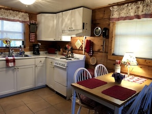 Una cocina con gabinetes blancos, una estufa y una mesa de comedor con individuales rojos.
