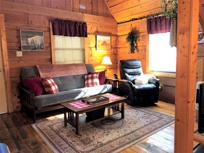 A cozy cabin interior with a sofa, armchair, and a coffee table. - Romantic Log Cabin with Hot Tub near Cherokee National Forest, Tennessee (Coker Creek)
