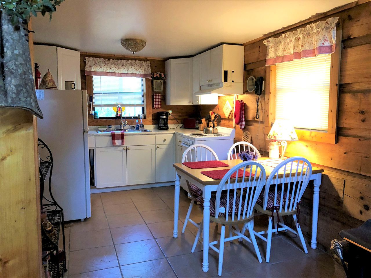 A compact kitchen with white cabinets, a dining table with chairs, and a window with blinds.