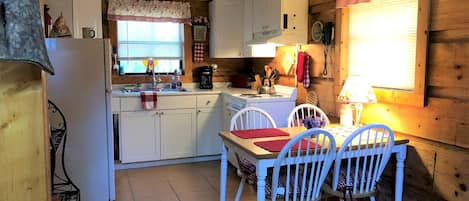 A compact kitchen with white cabinets, a dining table with chairs, and a window with blinds.
