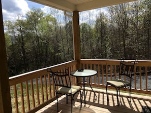Une terrasse couverte, dotée d’une table et de chaises, qui offre une vue sur une zone boisée.