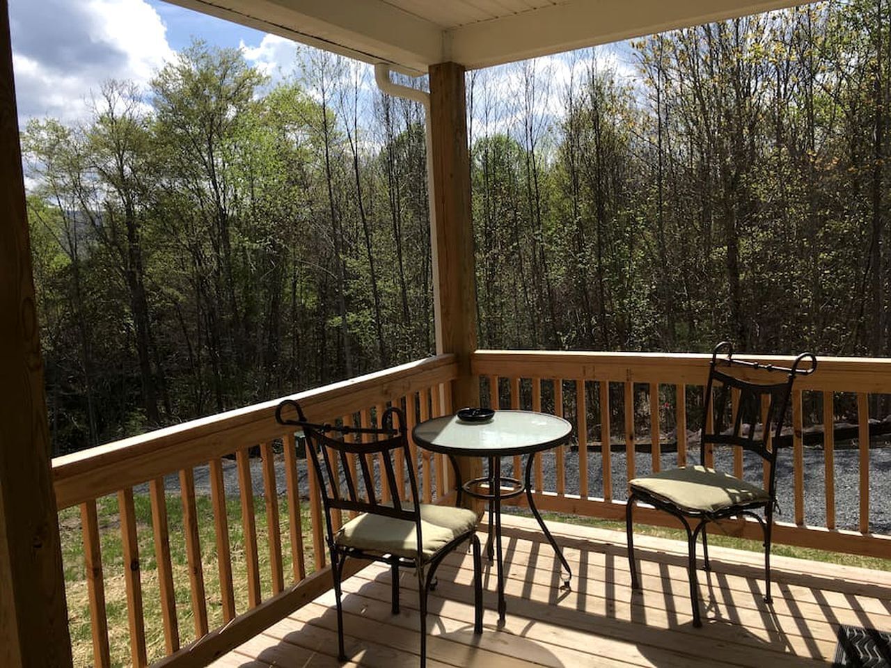 A covered deck with a table and chairs, overlooking a forested area.