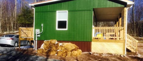 Un edificio pequeño, de color verde, con una terraza de madera y una sola ventana.