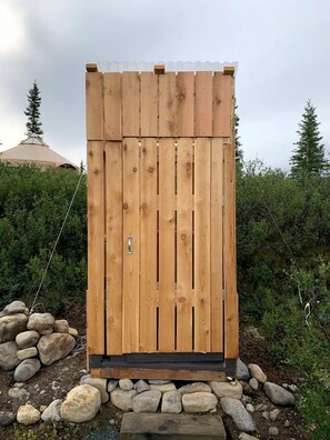 A wooden structure with a door, surrounded by rocks and greenery. - Peaceful Denali Accommodation for Yurt Glamping in Alaska (Cantwell)