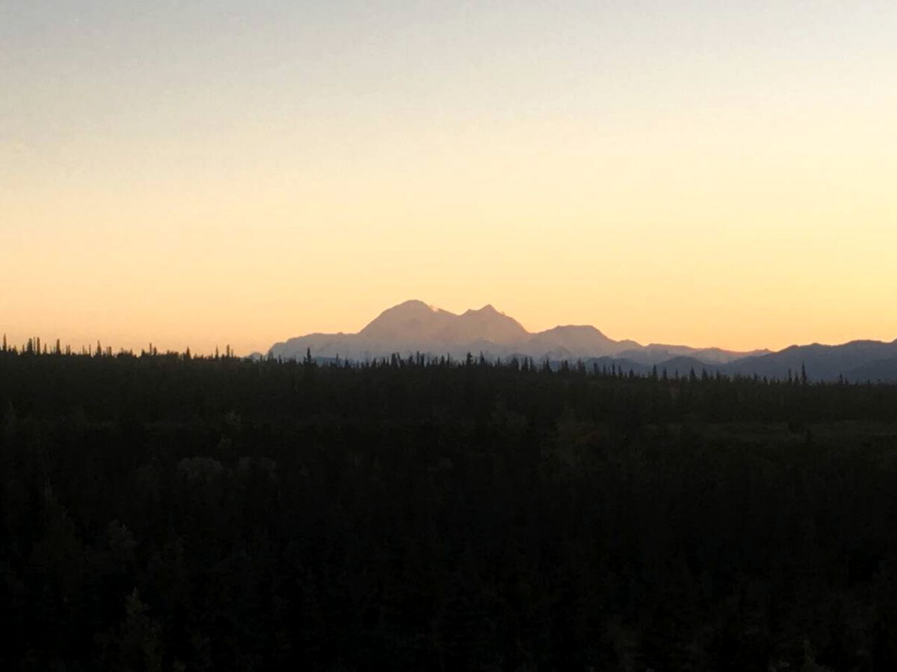 Eine gebirgige Landschaft mit bewaldetem Vordergrund und blauem Himmel.
