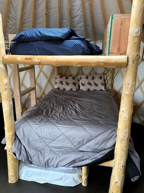 A wooden bunk bed with a grey quilted mattress and patterned pillows.