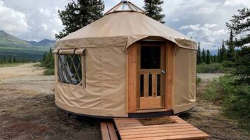 En yurt med en trædør, en lille veranda og et vindue.