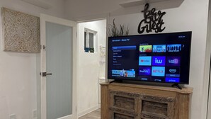 Een televisie op een houten standaard in een kamer met een deur, een wand met een decoratief bord en een bloemenbedekking.