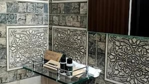 A bathroom with a white sink, decorative tiles, and a glass shelf with toiletries. - White Dove Luxurious Boutique Hotel (Mikir Para Chakardoi)
