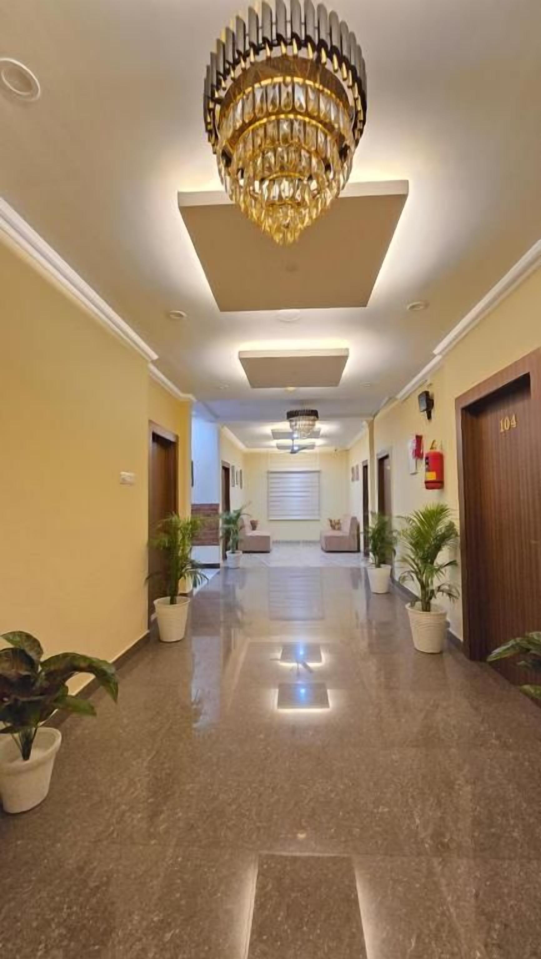A hotel corridor with a chandelier, potted plants, and a clean, polished floor.