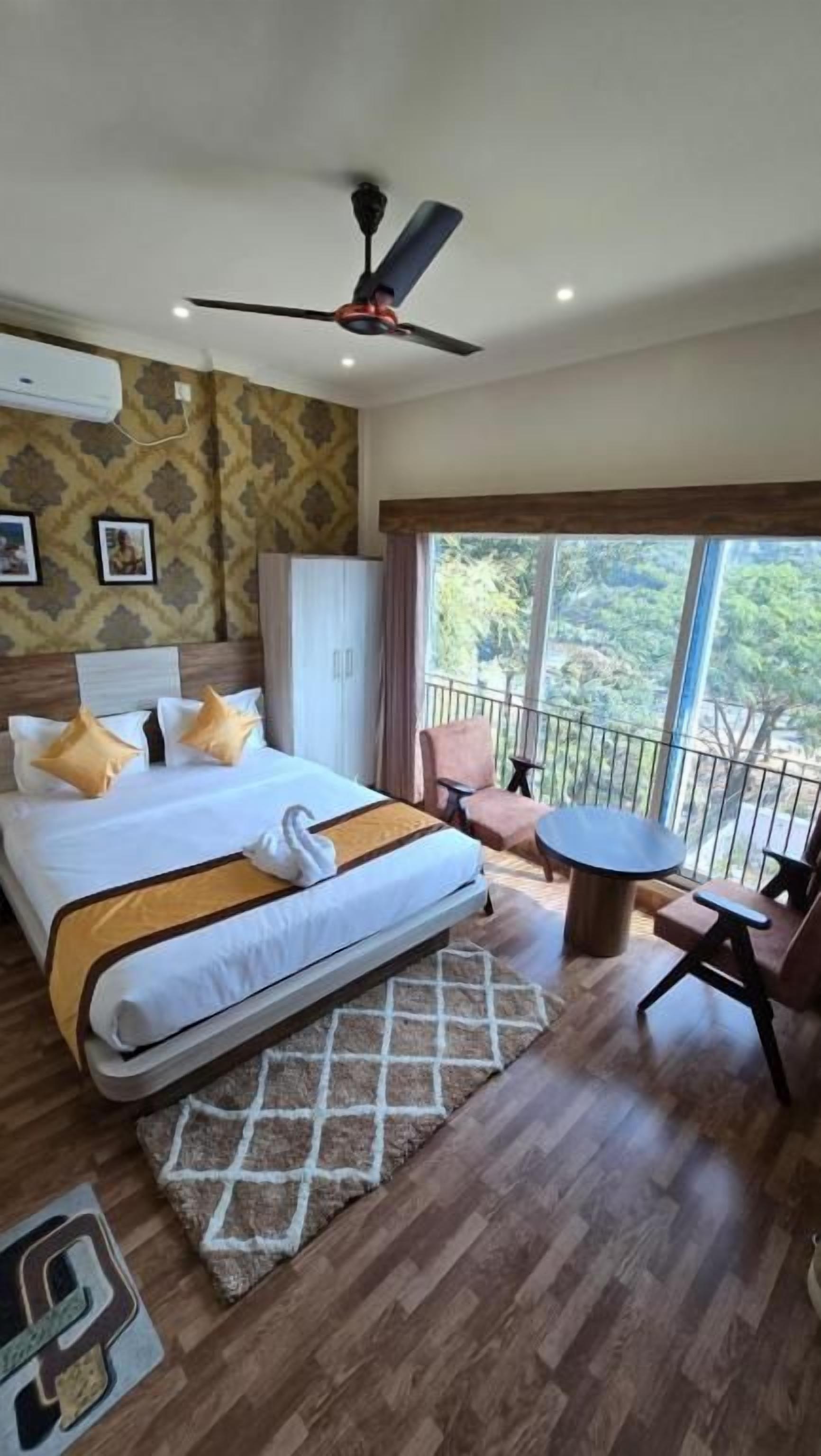 Une chambre d’hôtel avec un lit, un ventilateur de plafond, un balcon avec une chaise et une vue sur l’extérieur.