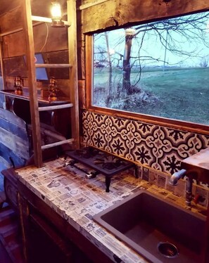 A rustic kitchen with a wooden countertop, a gas stove, and a window with a view of a grassy field. - Rustic Container Accommodation for Glamping in Kentucky (Owenton)
