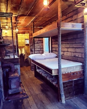 A rustic wooden cabin with bunk beds, a vintage stove, and a wooden floor.