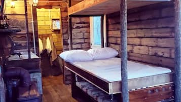 A rustic wooden cabin with bunk beds, a vintage stove, and a wooden floor.