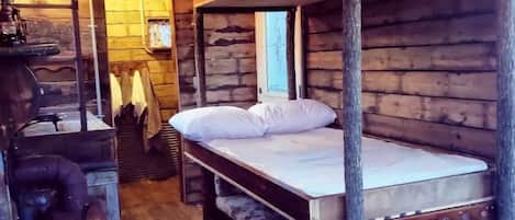 A rustic wooden cabin with bunk beds, a vintage stove, and a wooden floor.