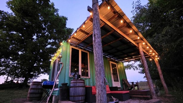 A rustic cabin with a wooden porch, a large barrel, and a potted plant.