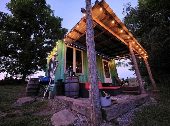 A rustic cabin with a wooden porch, a large barrel, and a potted plant.