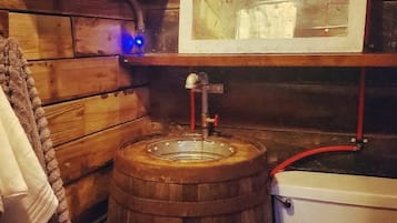 A rustic bathroom with a wooden barrel sink, a toilet, and a mirror above the sink.