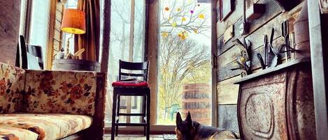 L'interno accogliente di un rifugio rustico, con pavimento in legno, un divano, una poltrona e un cane che riposa vicino a una finestra.