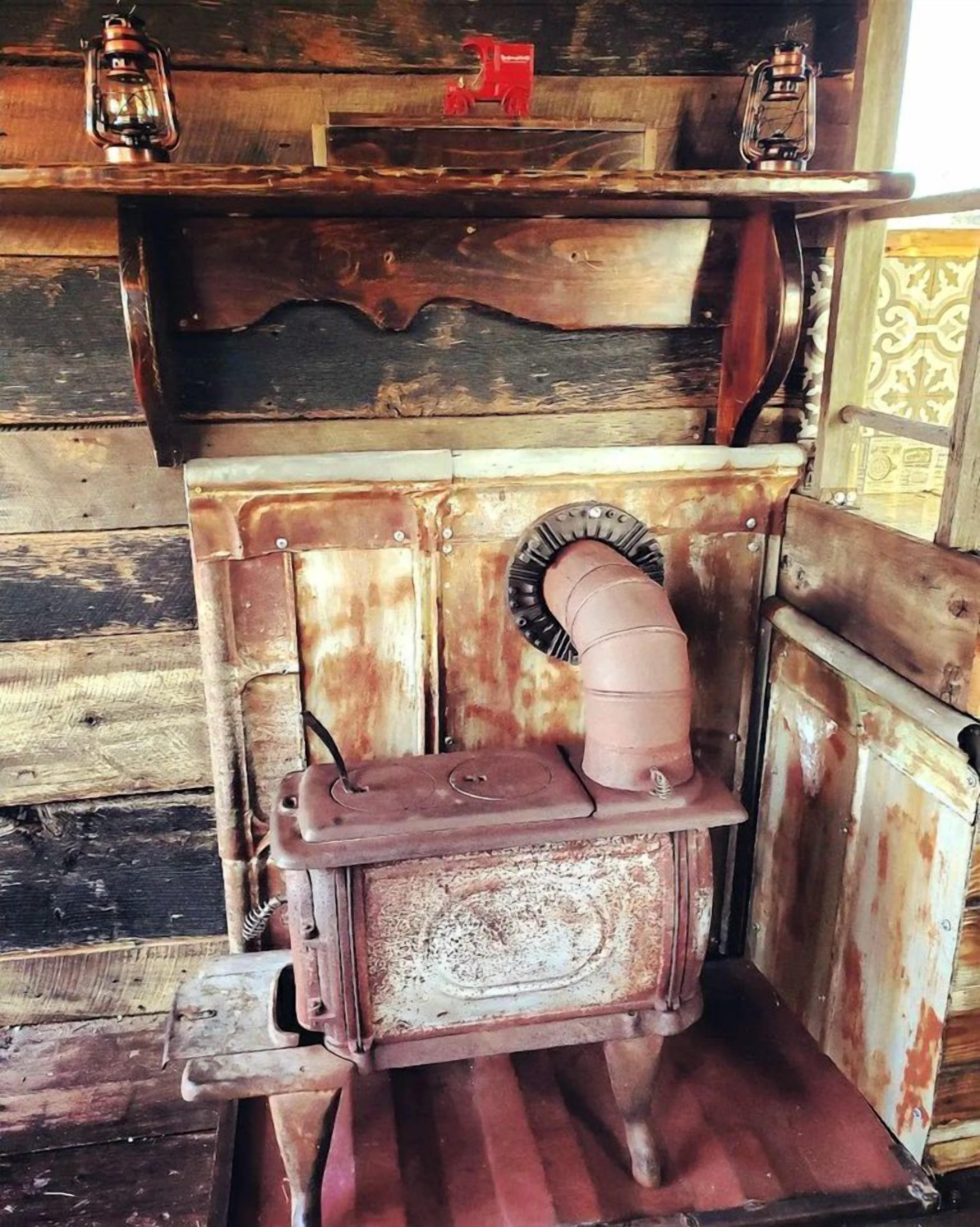 A rustic wooden stove with a chimney, a shelf above it, and a decorative item on the shelf.