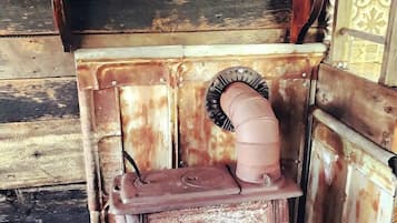 A rustic wooden stove with a chimney, a shelf above it, and a decorative item on the shelf.