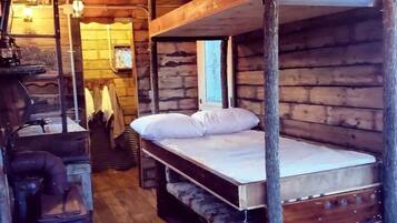 A rustic wooden cabin with bunk beds, a vintage stove, and a wooden floor.