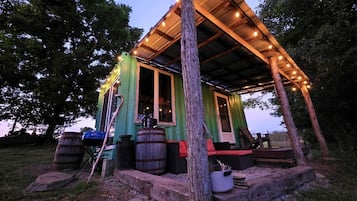 A rustic cabin with a wooden porch, a large barrel, and a potted plant.
