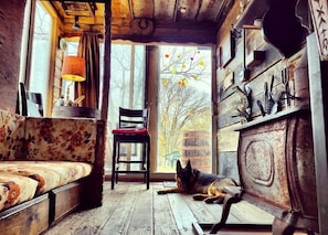 A rustic cabin interior with a wooden floor, a sofa, a chair, and a dog resting near a window.