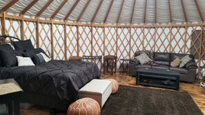 A yurt interior with a bed, sofa, ottoman, and a small table. - Luxurious Lakefront Yurt Rental for a Romantic Getaway near Grapevine, Texas (Southlake)