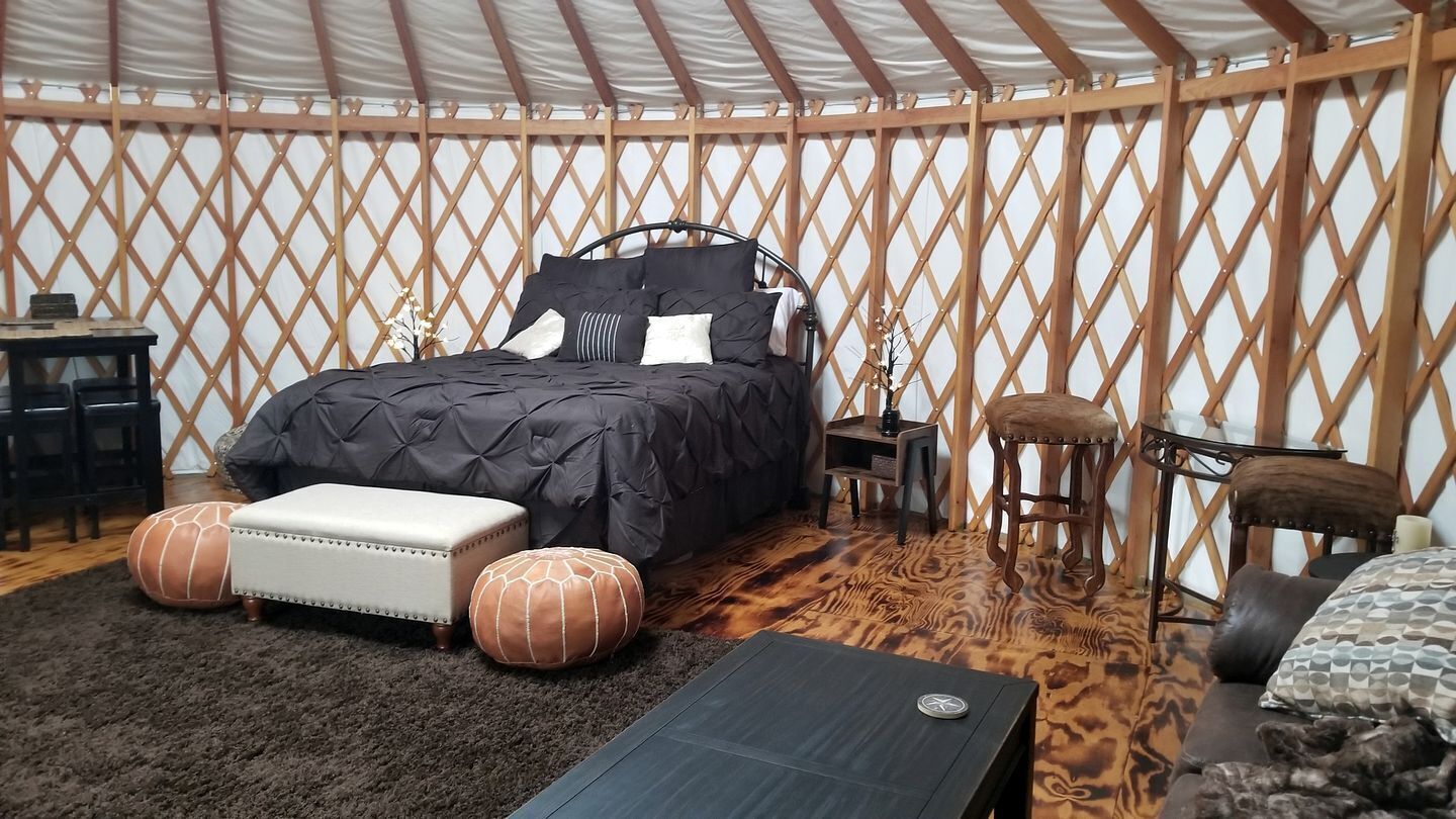 A room with a bed, ottomans, a small table, and a chair.