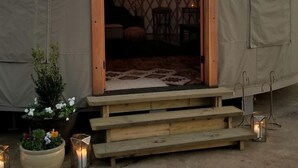 Ein großes Zelt mit einer Holztür, einer kleinen Veranda und einem Blumentopf davor.