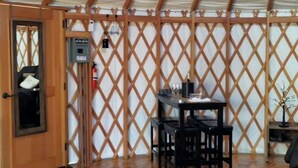 Ein Zimmer mit Holztür, Tisch mit Stühlen, kleinem Teppich und Holzboden.