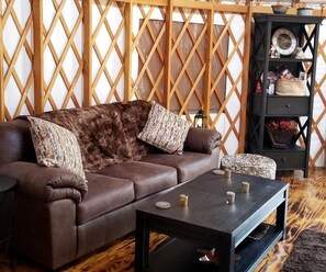 A brown leather sofa with patterned cushions, a dark wooden coffee table, and a black side table with a clock and decorative items.