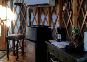 Cocina compacta con refrigerador, un taburete de madera y una mesa pequeña con utensilios de cocina.