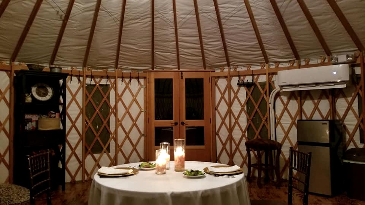 A round table with candles, plates, and cutlery in a tent with wooden lattice walls and a central door.