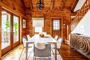 A wooden cabin interior with a dining table, chairs, a chandelier, and a spiral staircase. - Modern, Cozy, Idyllic Log Cabin Secluded on 6 Serene Acres, Stone Ridge, New York (Stone Ridge)