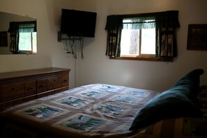 A bedroom with a bed, dresser, TV, and windows. - Rustic Family Cabin Rental with a Fire Pit near Wisconsin Dells (Tomah)